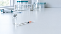 Unlabeled glass vial and U-100 insulin syringe on a white laboratory bench with laboratory glassware in the background